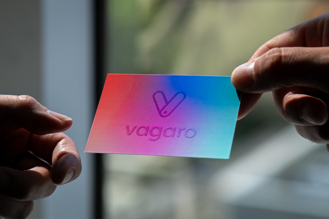 Two hands hold a rainbow gradient card with the Vagaro logo embossed in the center.