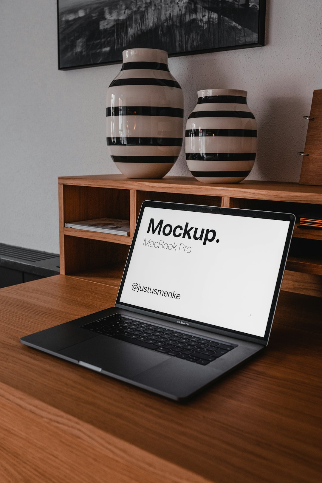 MacBook Pro open on a wooden desk, screen shows a mockup with the text 'Mockup. MacBook Pro' and '@justusmenke'.