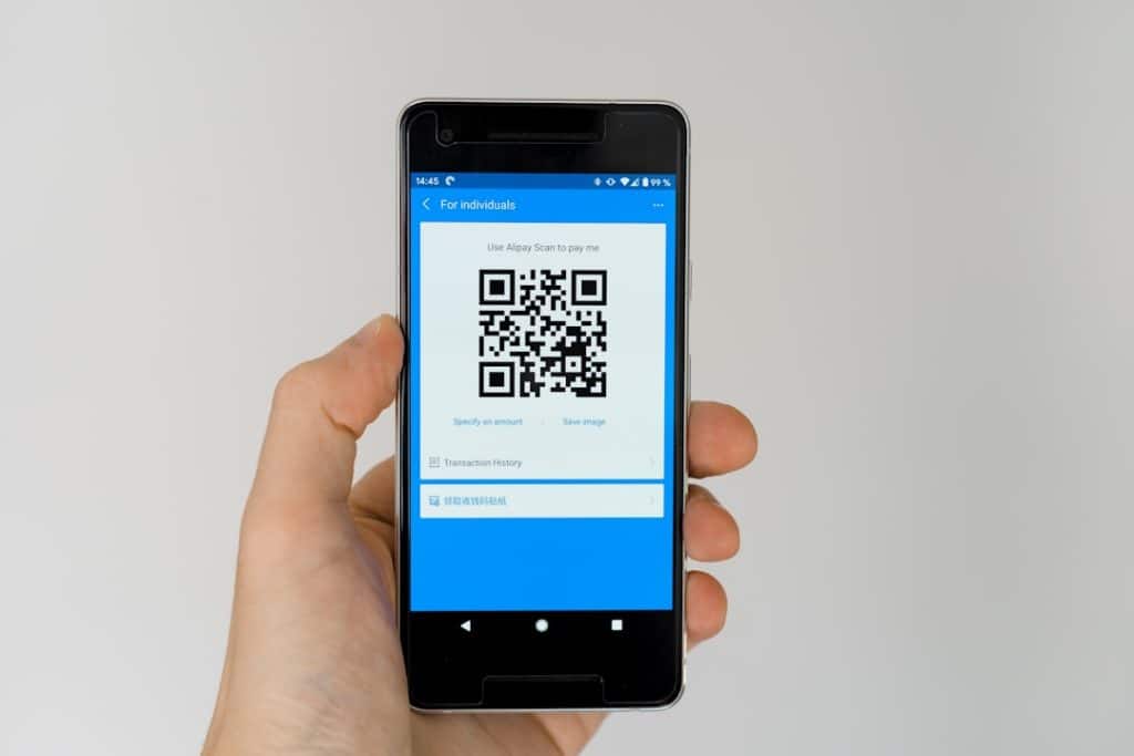 Hand holding a smartphone displaying a blue payment app screen with a large QR code for payment
