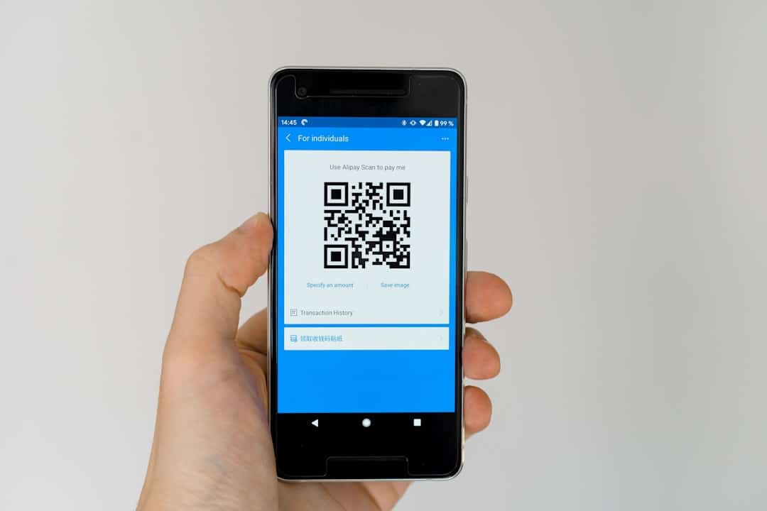 Hand holding a smartphone displaying a blue payment app screen with a large QR code for payment