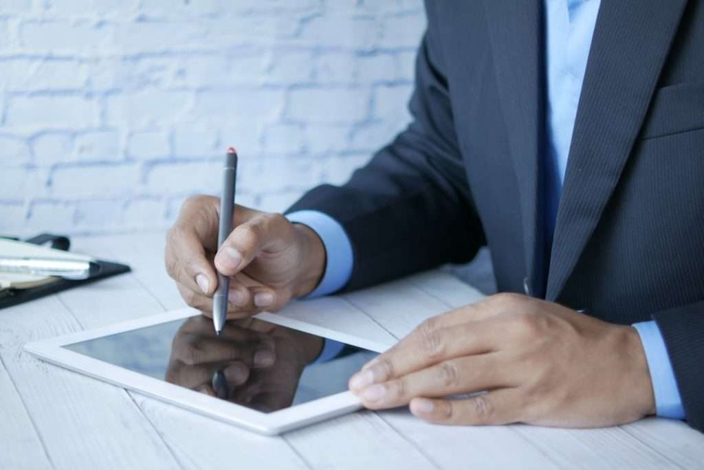 a man in a suit writing on a tablet international business meeting on laptop passport verification online remote identity check global document signing - AI Bud
