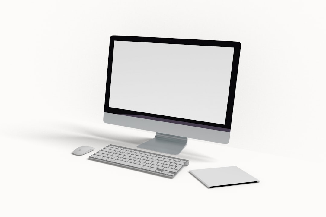 All-in-one desktop computer with wireless keyboard and mouse on a white desk, plus a closed notebook nearby.