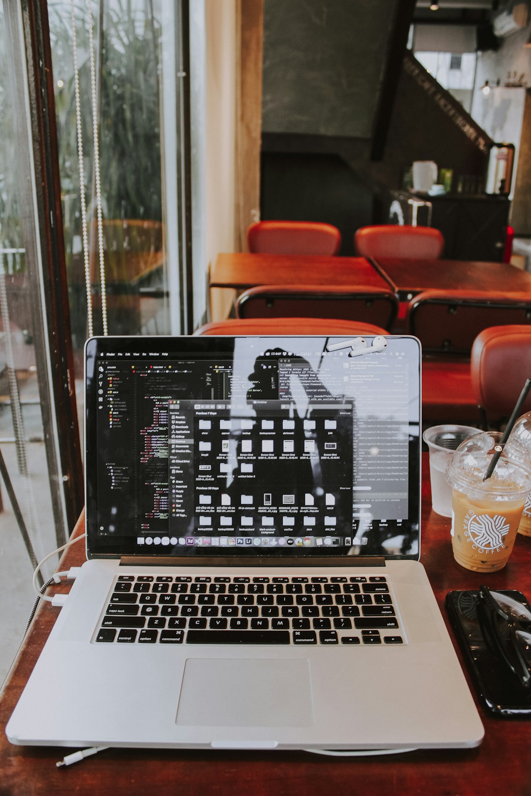 Open laptop on a wooden cafe table with an iced coffee to the right and red chairs in the background.