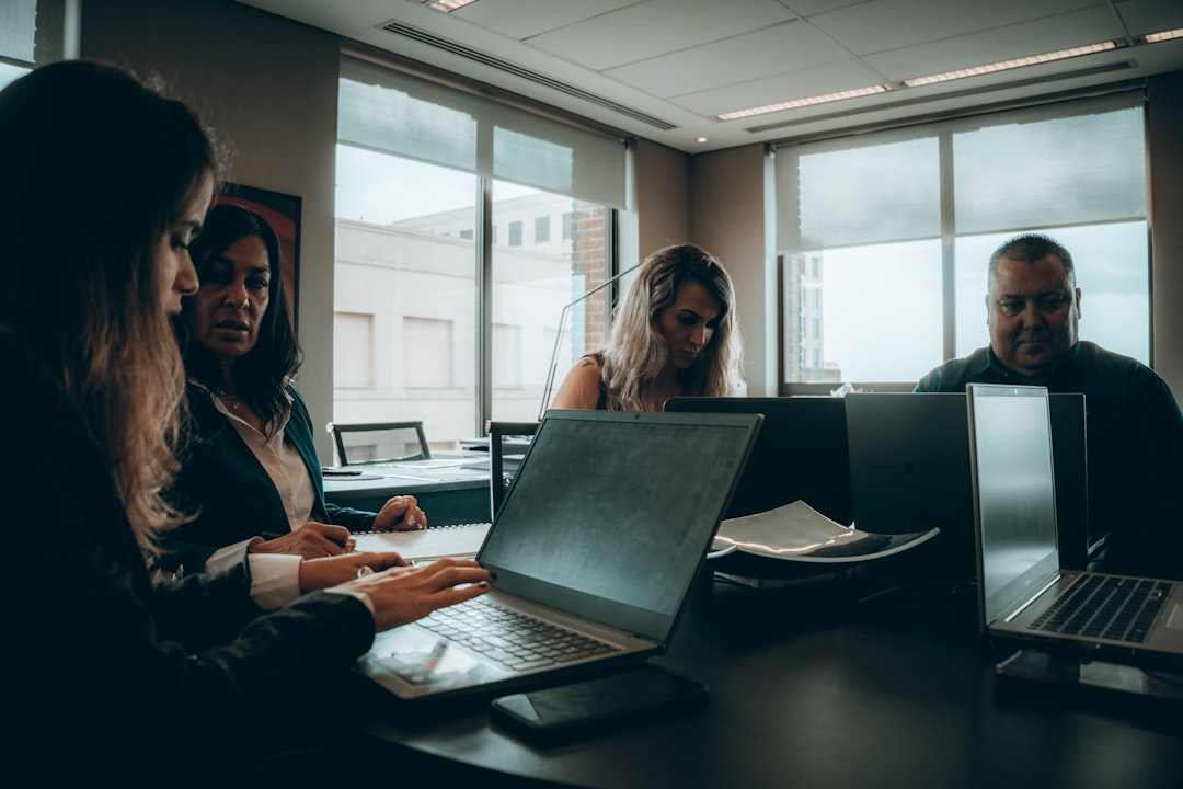 Four professionals collaborate around a conference table with laptops in a bright, modern office.