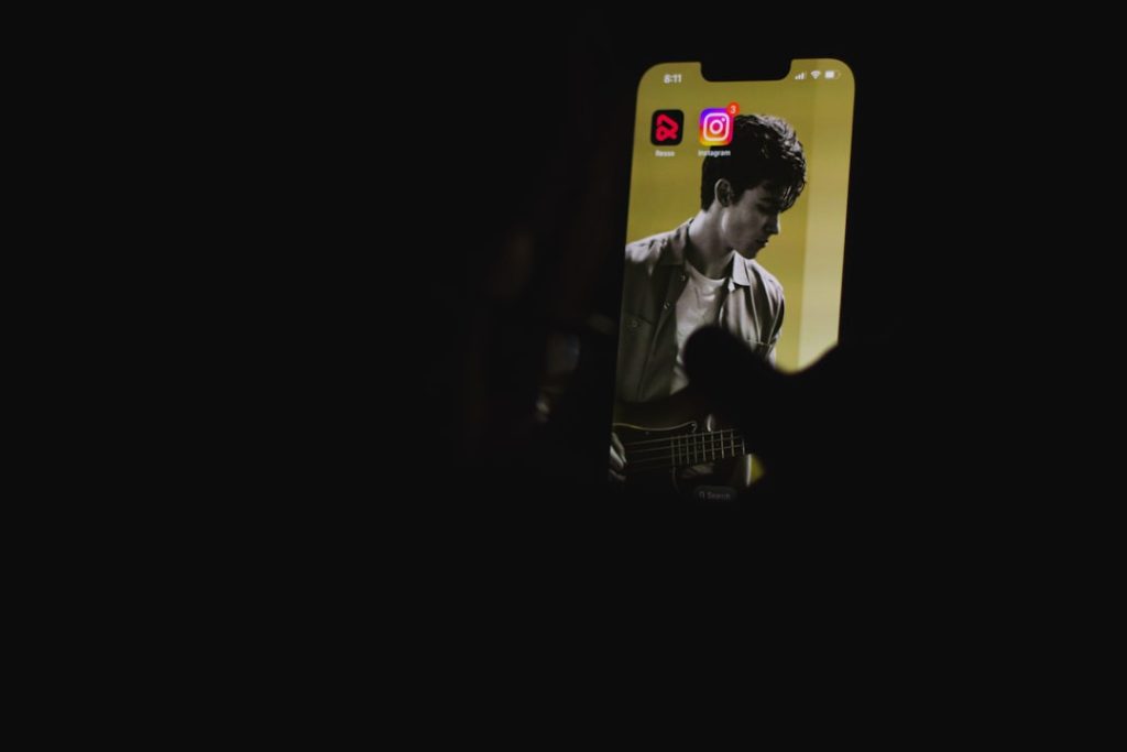 Phone held in a dark setting displaying a musician image on the screen, with two app icons at the top.
