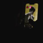 Phone held in a dark setting displaying a musician image on the screen, with two app icons at the top.