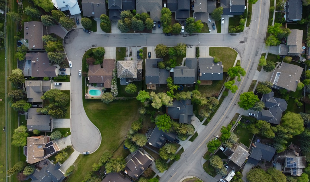 Aerial view of a suburban neighborhood with tree-lined streets, houses, and a cul-de-sac featuring a small backyard pool nearby.
