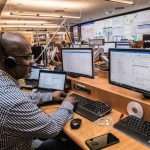 Operator wearing a headset at a multi-monitor command center, monitoring dashboards and emails.