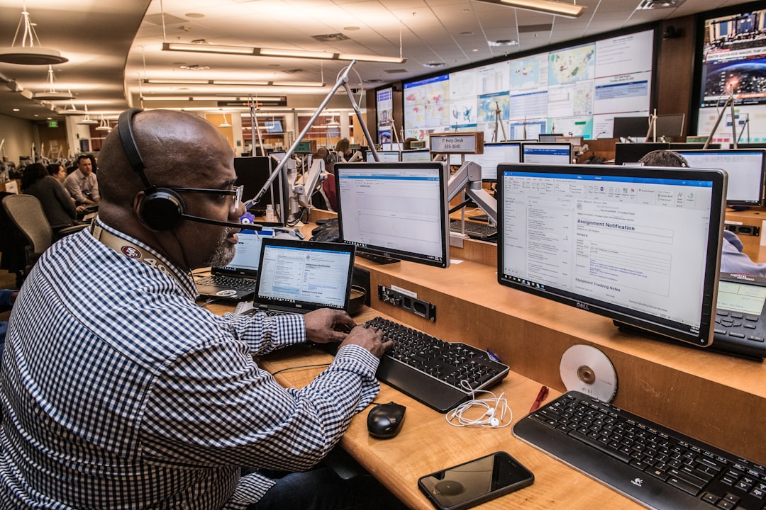 Operator wearing a headset at a multi-monitor command center, monitoring dashboards and emails.