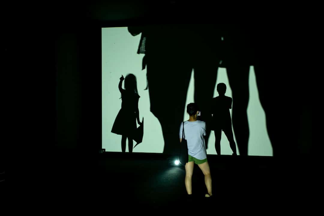 man in white t-shirt and green shorts standing in front of people students animation virtual classroom - AI Bud