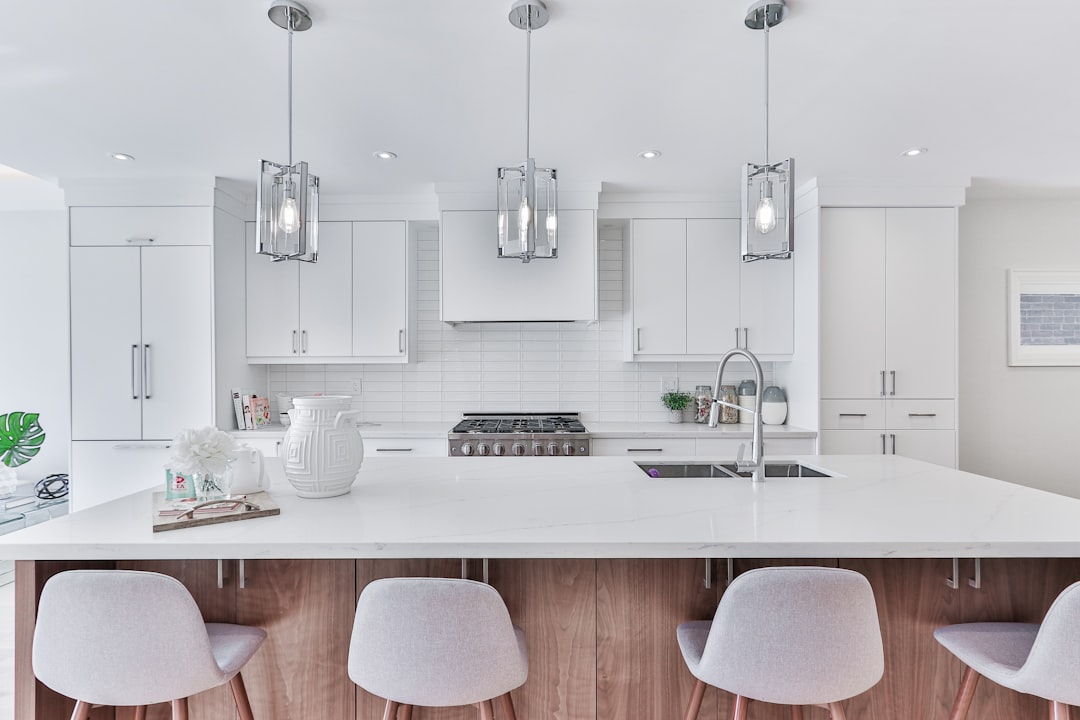 Bright, modern kitchen with white cabinets, stainless steel range, and a large marble island under three pendant lights, with light gray stools along the island.