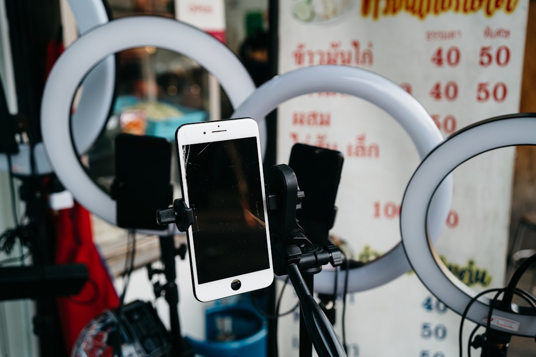 Phone mounted on a tripod between circular LED ring lights for filming or livestreaming.
