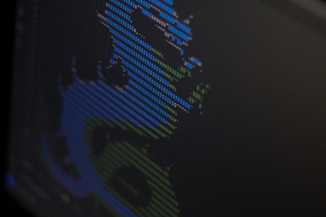 Close-up of a monitor displaying colorful ASCII-style code with blue and green characters on a dark background.