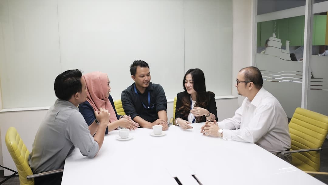 a group of people sitting around a white table team meeting employee management office discussion - AI Bud