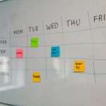 Whiteboard weekly content schedule with Mon–Fri columns and rows for Twitter, TikTok, Instagram, Facebook; colorful sticky notes mark topics across days.