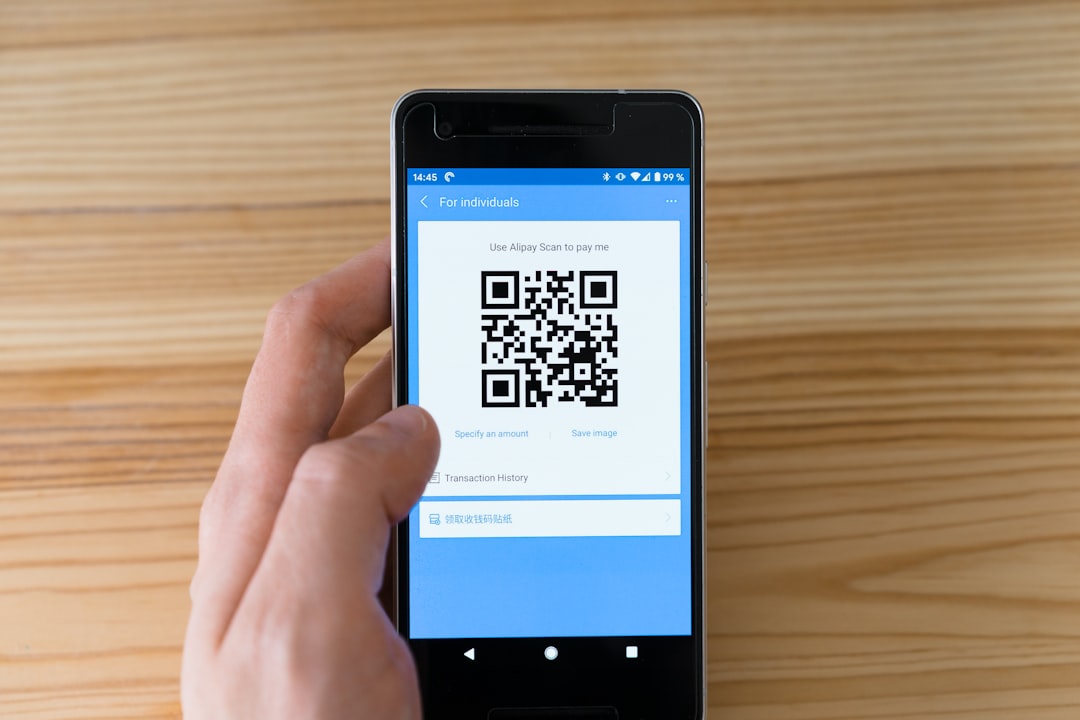 Hand holding a smartphone that displays a QR code for payment via Alipay/receive payment.