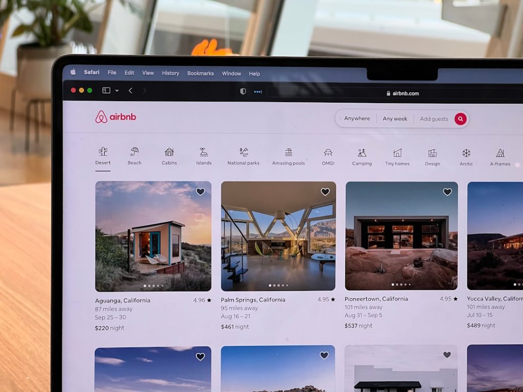 Laptop screen showing Airbnb homepage with listings, logo, and search bar in view.