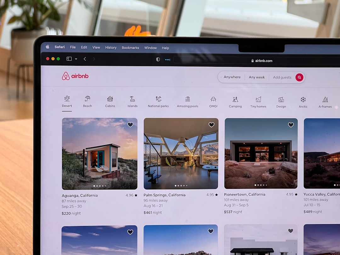 Laptop screen showing Airbnb homepage with listings, logo, and search bar in view.