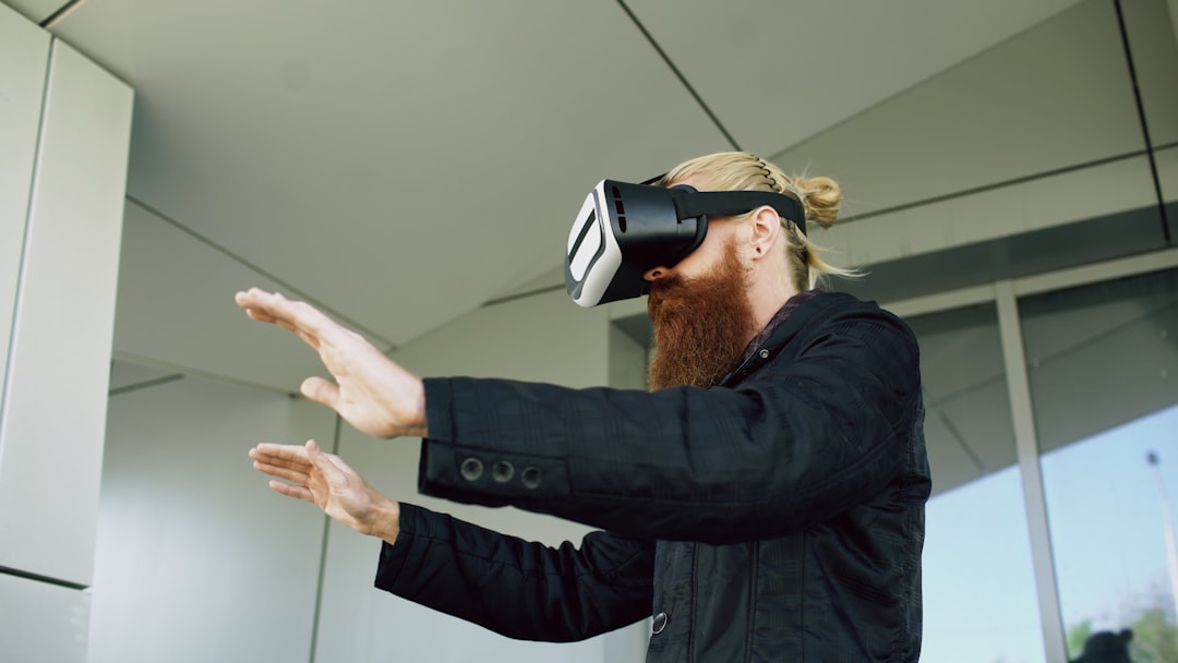 Bearded man wearing a VR headset extends his hands forward indoors, engaged in virtual reality.