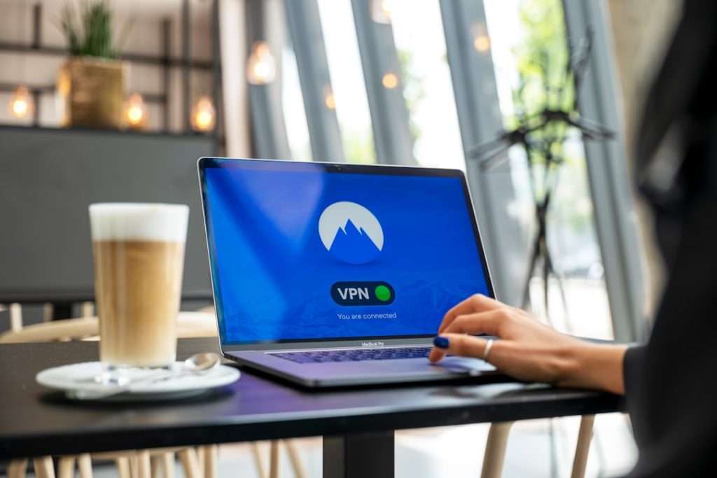 Laptop on a cafe table with a VPN screen showing 'You are connected' and a mountain logo.