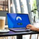 Laptop on a cafe table with a VPN screen showing 'You are connected' and a mountain logo.