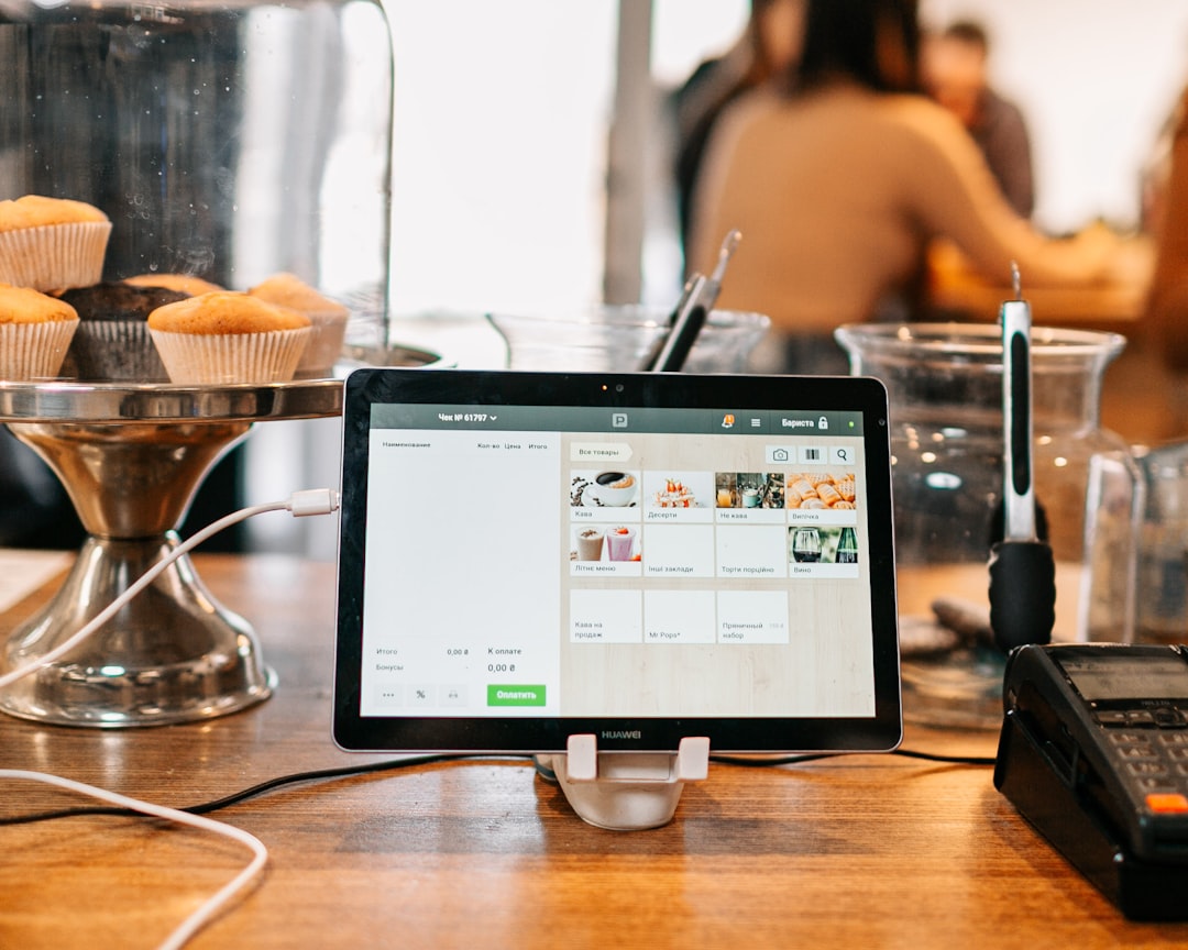 Tablet POS on a cafe counter showing a menu while pastries sit in a display behind it.