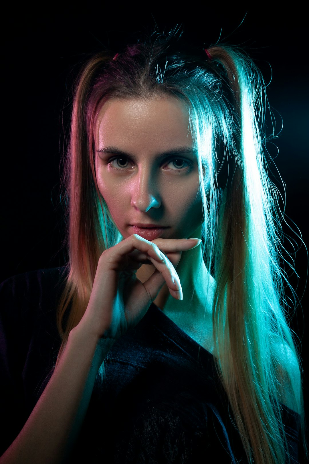 Portrait of a young woman with long blond hair, lit by blue and pink neon lights against a dark background.