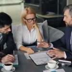 Three professionals in a meeting, reviewing printed charts and notes on a conference table.