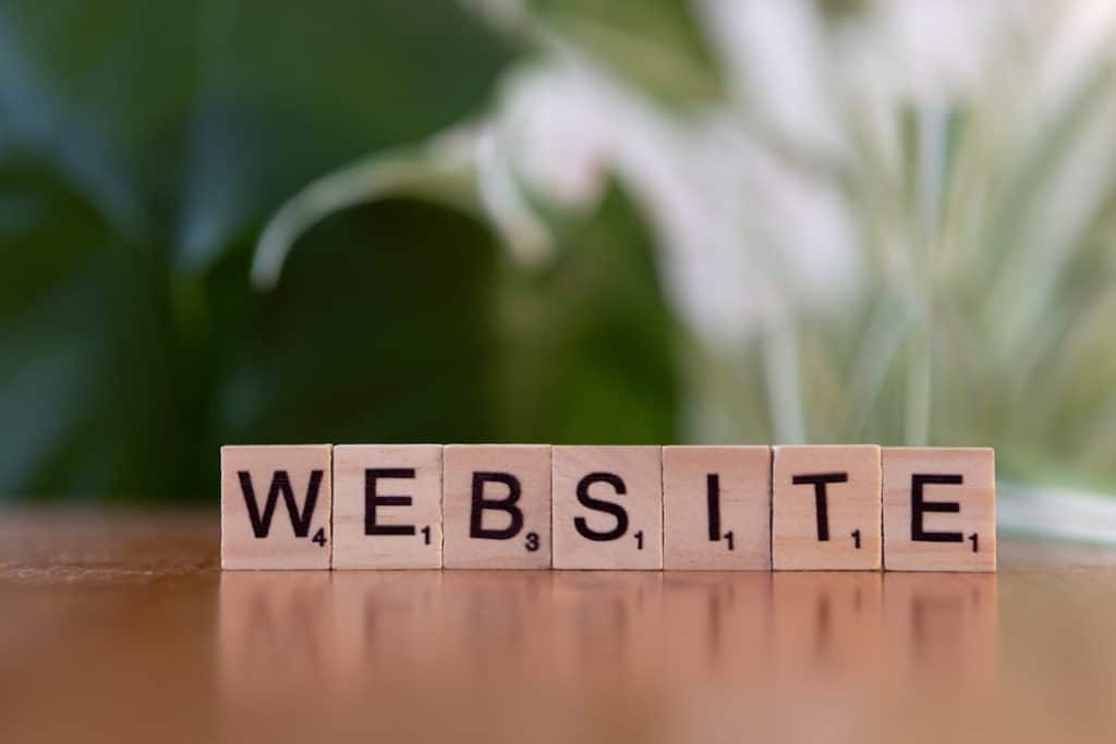 Wooden letter blocks spell WEBSITE on a table with a soft green background.