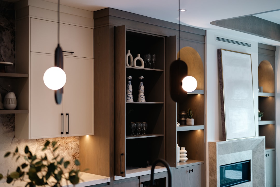 Contemporary kitchen wall with white and wood cabinets, open shelves showing vases and glassware, pendant lights.