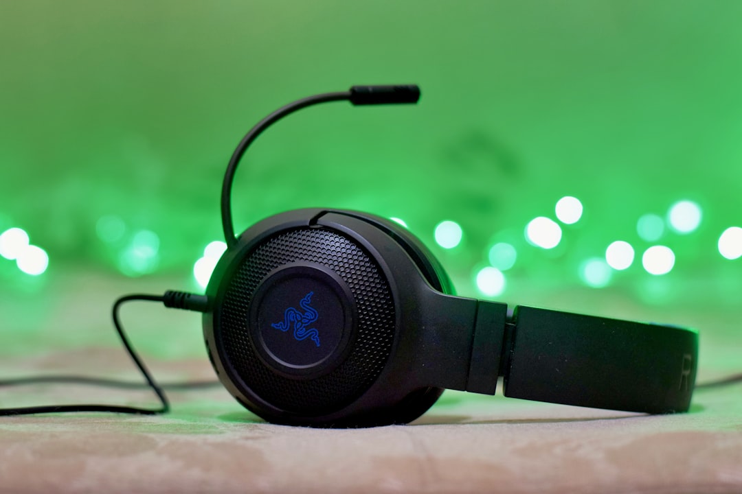 Black gaming headset with a mic, lying on a surface with green bokeh lights in the background, Razer logo visible on the ear cup.