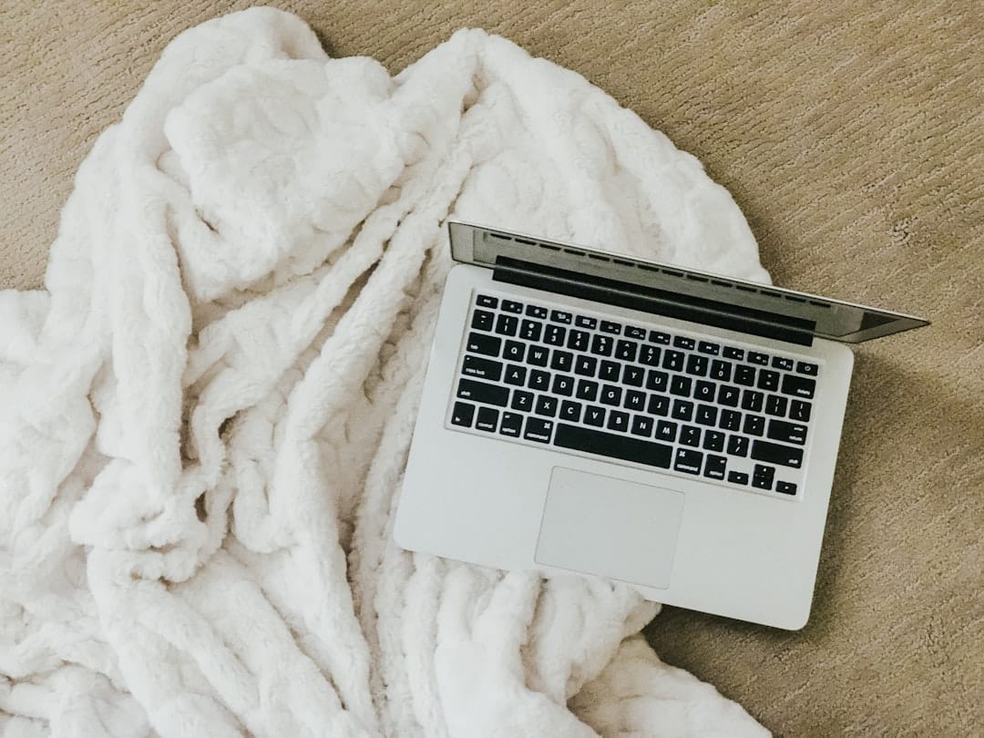MacBook on white comforter beginner blogger writing on laptop cozy environment - AI Bud