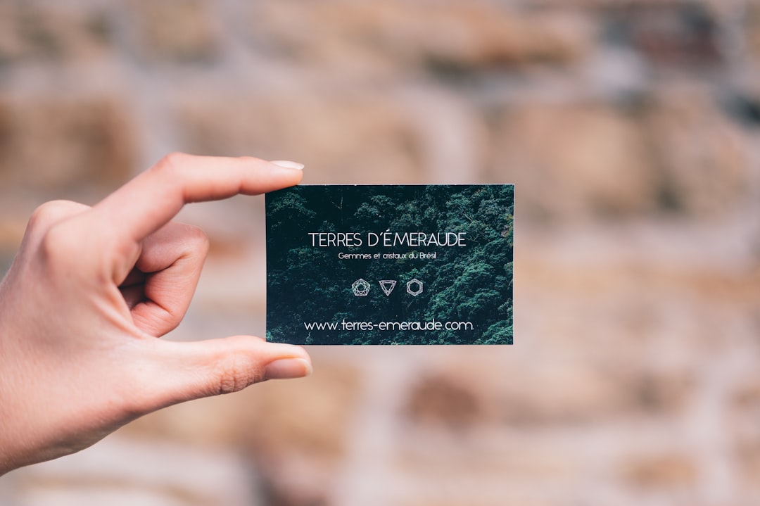 Hand holding a dark green business card that reads TERRES D'ÉMERAUDE, with gems and a Brazilian theme, and a website address visible.