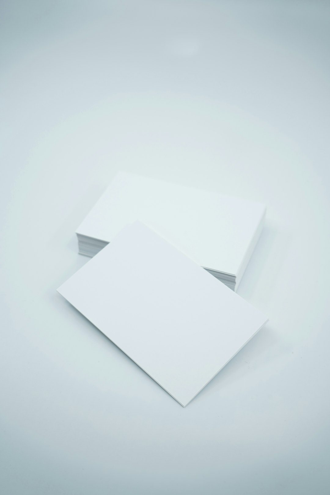 Two blank white business cards on a pale blue surface, one resting atop the other at a slight angle.
