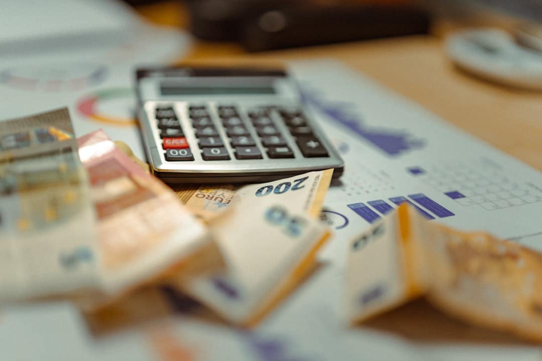 Person uses a calculator amid scattered euro banknotes and receipts on a desk, suggesting budgeting or accounting work.