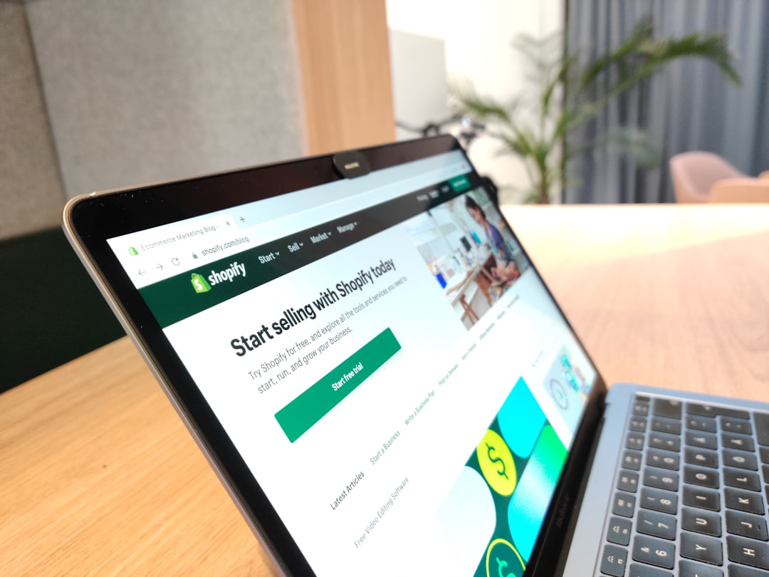 Tablet on a wooden desk displaying the Shopify homepage with a green 'Start free trial' button on screen.