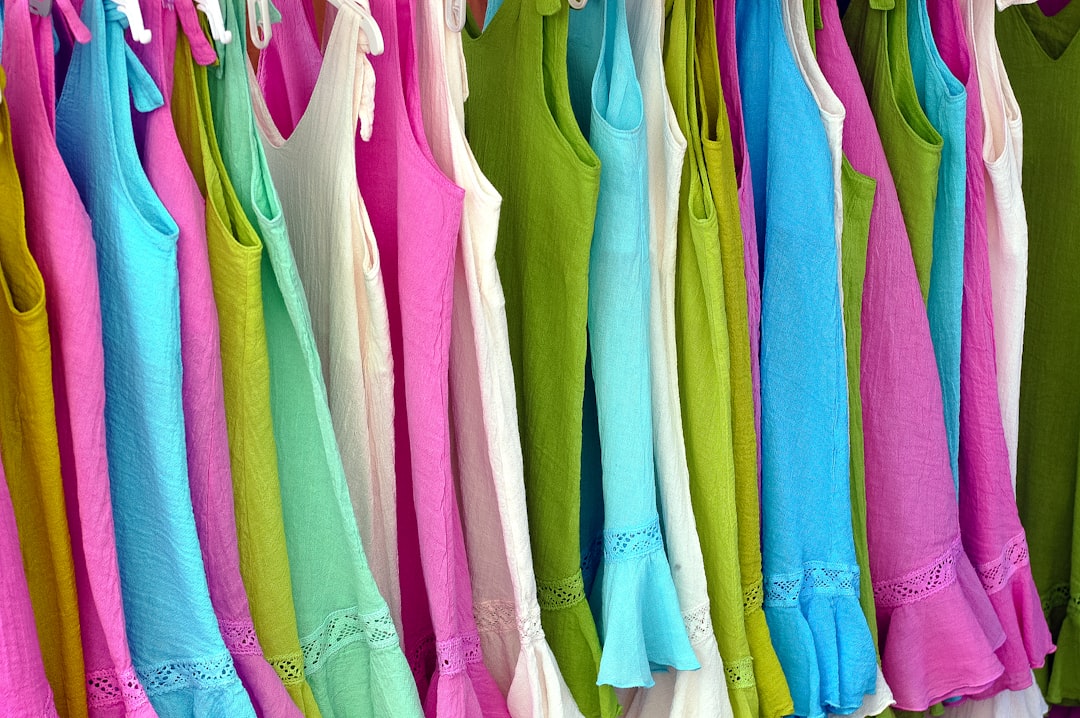 Row of bright colorful summer dresses hanging on a rack, in pink, blue, green, and white with lace trim.