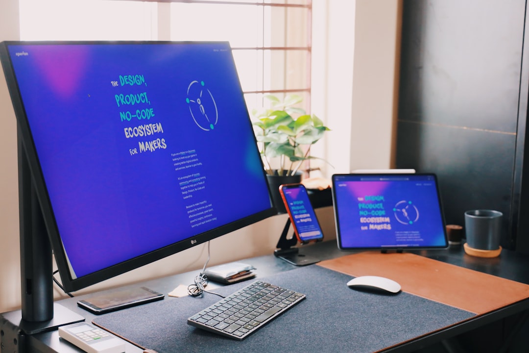 Desk workspace with a large monitor, tablet, and smartphone all displaying a blue design about design, product, no-code ecosystem for makers.