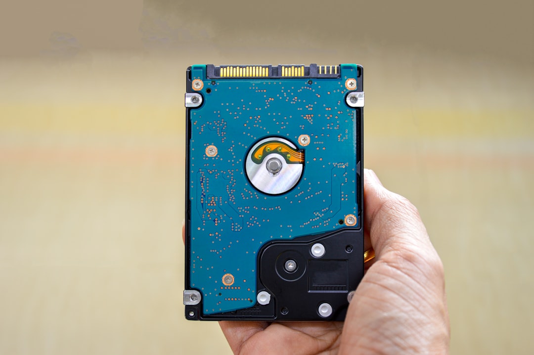Hand holding a 3.5-inch internal hard drive with a blue PCB and visible spindle, showing internal components while being examined.