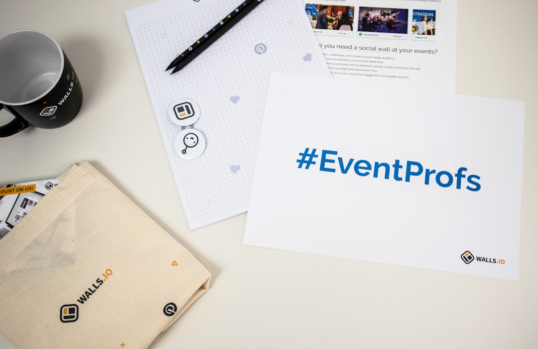 White card with the blue hashtag '#EventProfs' and Walls.io logo on the bottom-right, surrounded by office branding items and a mug on a desk toolset.