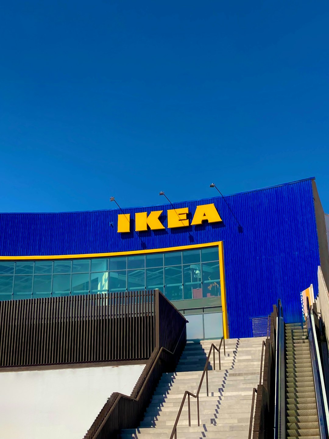 IKEA store with a blue facade and large yellow sign, at the top of concrete stairs with metal railings.