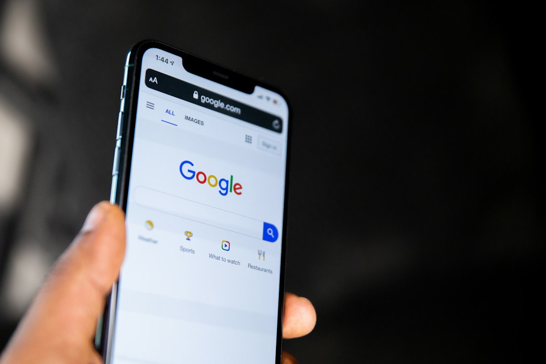 Hand holding a smartphone displaying the Google homepage with the search bar and navigation icons visible on screen.