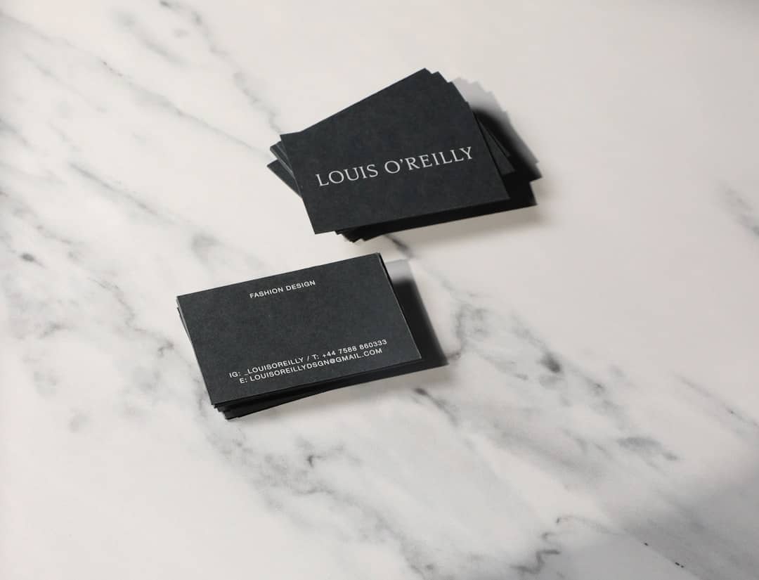 Black business cards on a white marble surface, displaying the name Louis O'Reilly and ‘Fashion Design’ text stack.