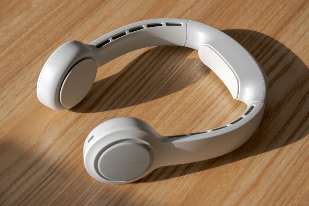 White over-ear headphones placed on a wooden table, showing the ear cups and headband in a curved position.
