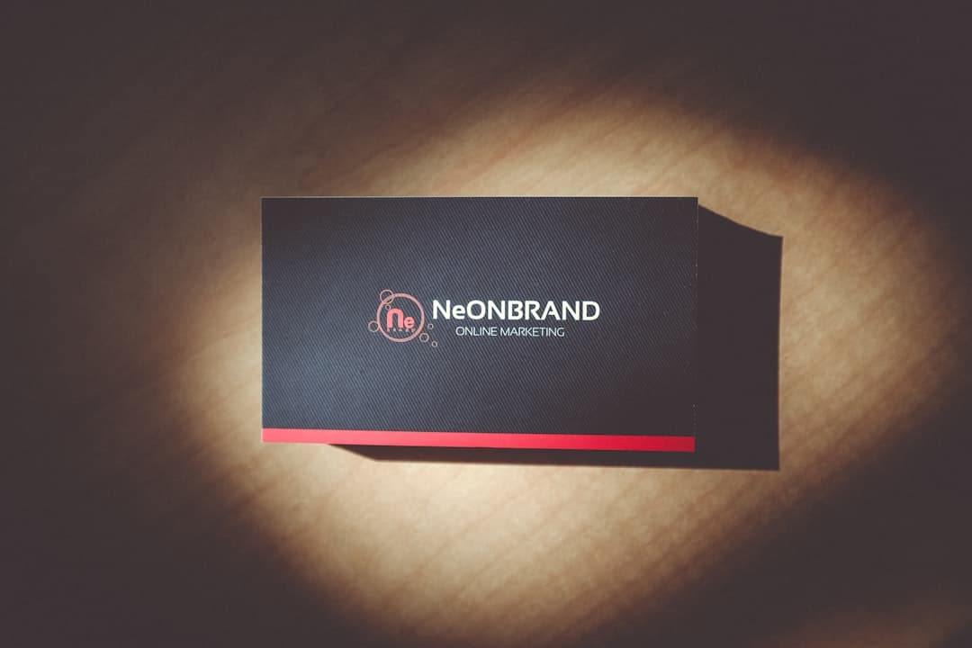 NeONBRAND Online Marketing business card on a dark surface with a pink circular logo and red bottom stripe.