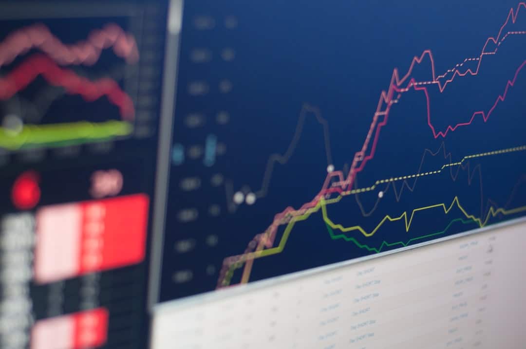 Multiple colorful line charts rising on a dark blue screen, representing stock market data and trends.