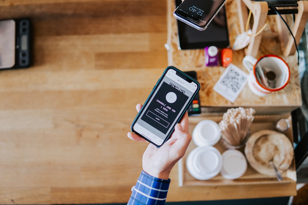 Person holding a smartphone showing a dark login screen with a 'Sign in' form at a coffee counter.