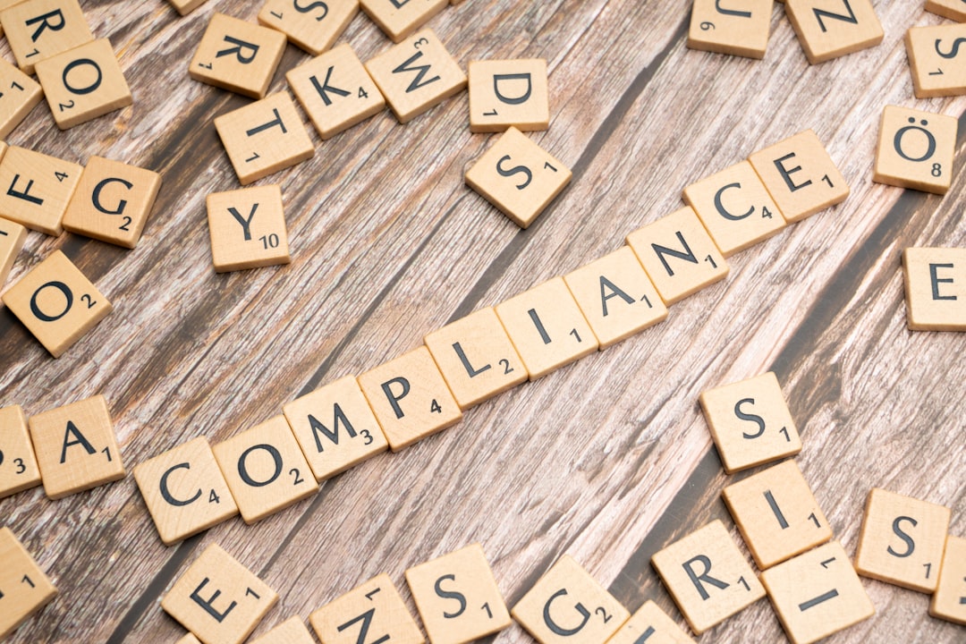 Scrabble tiles spell 'COMPLIANCE' on a wooden surface with some letters scattered around, symbolizing compliance and standards.