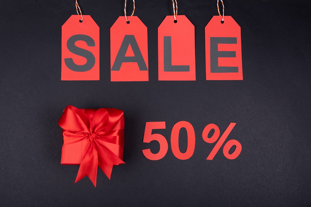 Four red sale tags spell 'SALE' above a red gift box on a dark background, with '50%' nearby to indicate discounts.