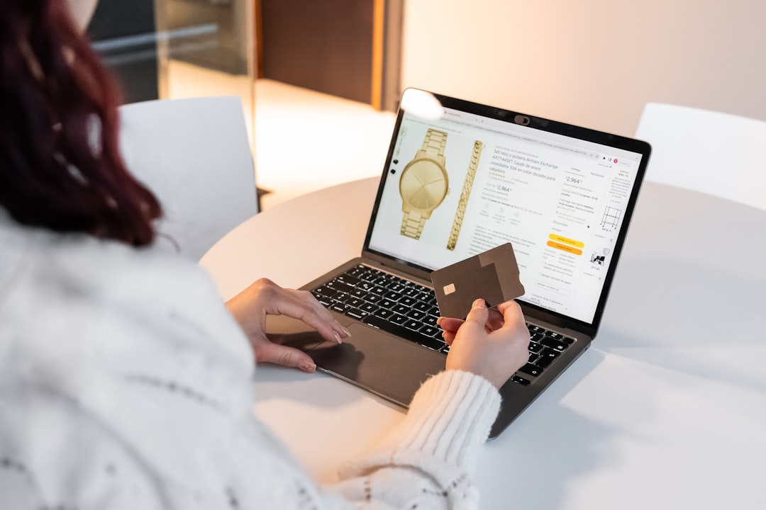 Person shopping for jewelry online, holding a credit card while viewing a gold watch on a laptop screen.